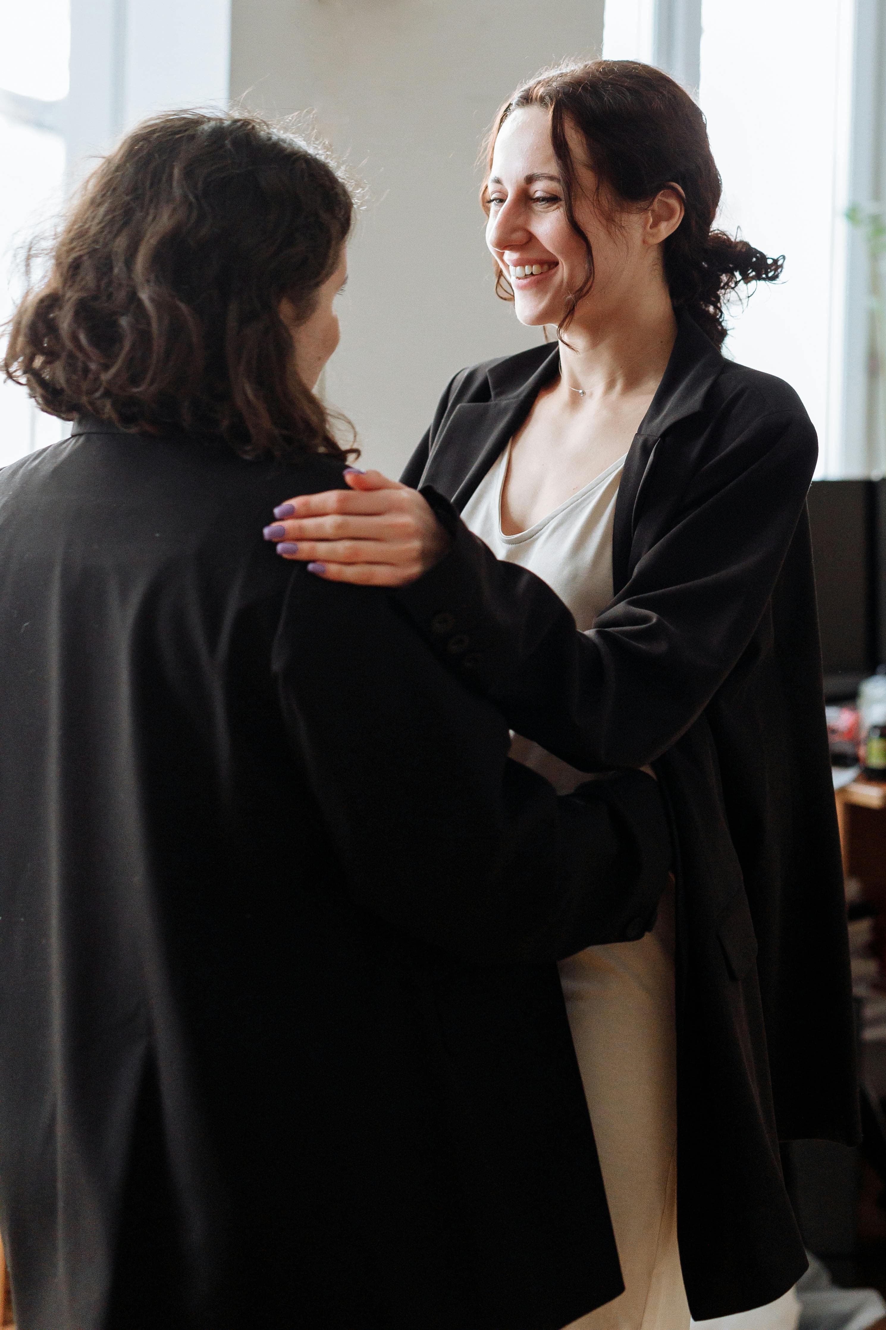 Two women facing each other warmly, one with hand on the others shoulder