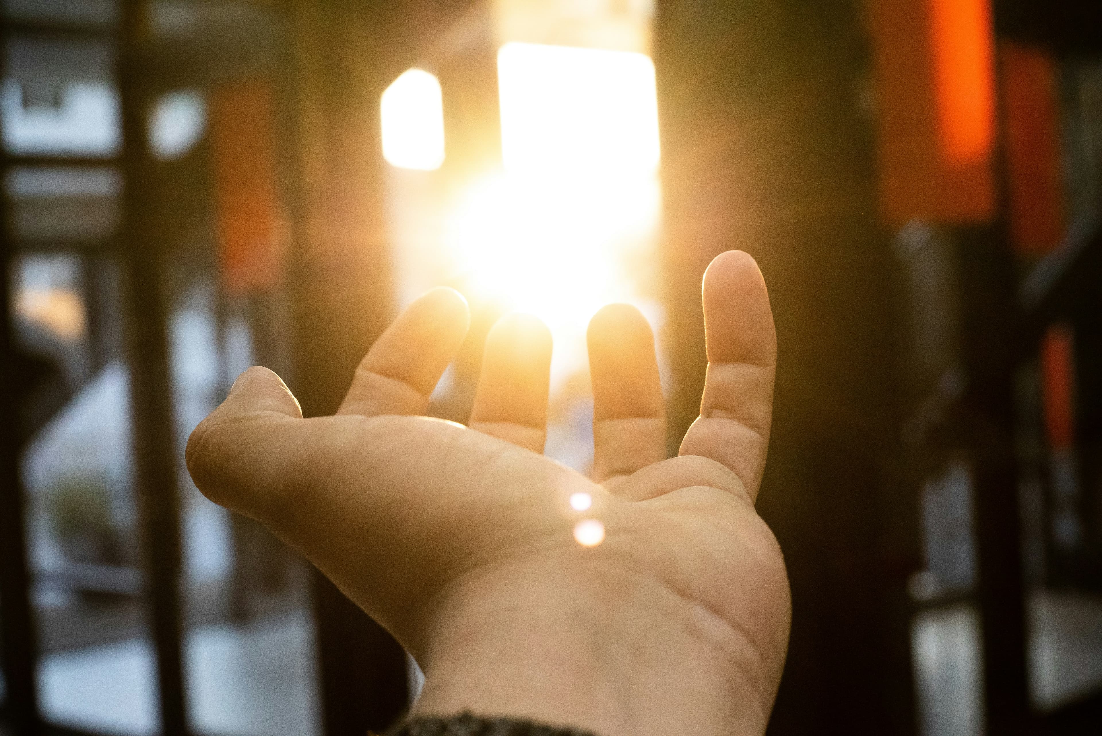 Hand reaching toward warm sunlight through a window